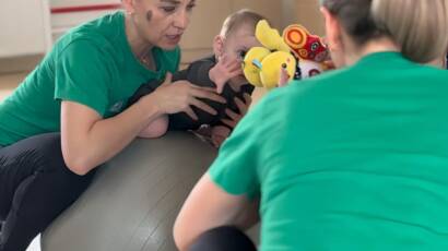 Kinetoterapeut efectuând stimulare senzorio-motorie cu bebeluș pe minge terapeutică