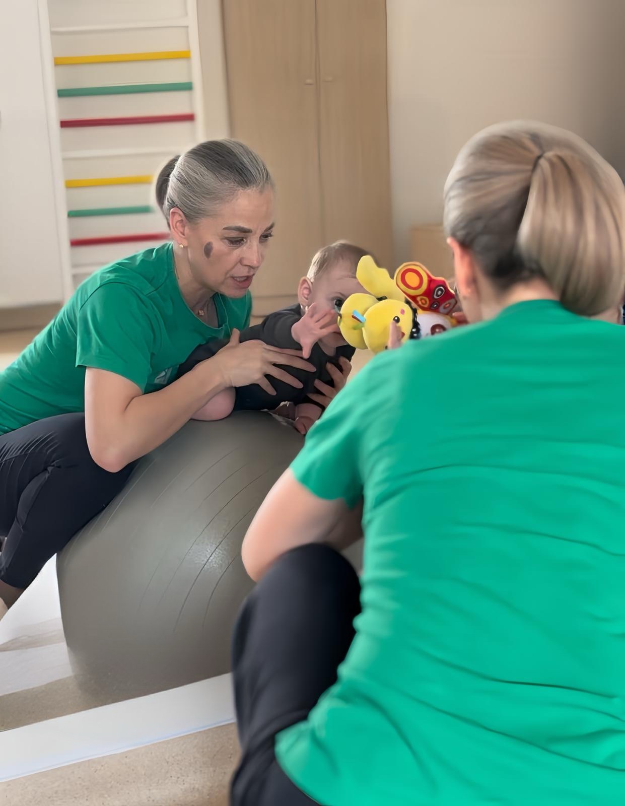Kinetoterapeut efectuând stimulare senzorio-motorie cu bebeluș pe minge terapeutică